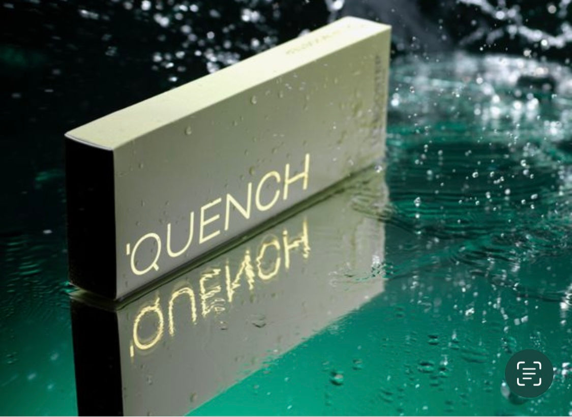 A product image featuring a card with the text 'QUENCH' on the front, placed against a background with water droplets and a green tint, suggesting hydration. Lip booster for hydration and fine lines on the lips